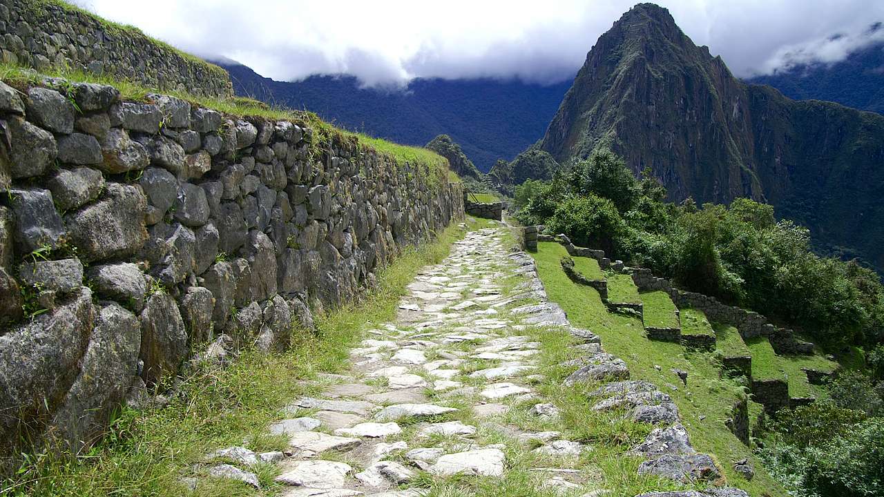 A stone path with rocks and grass with mountains in the background covered in clouds