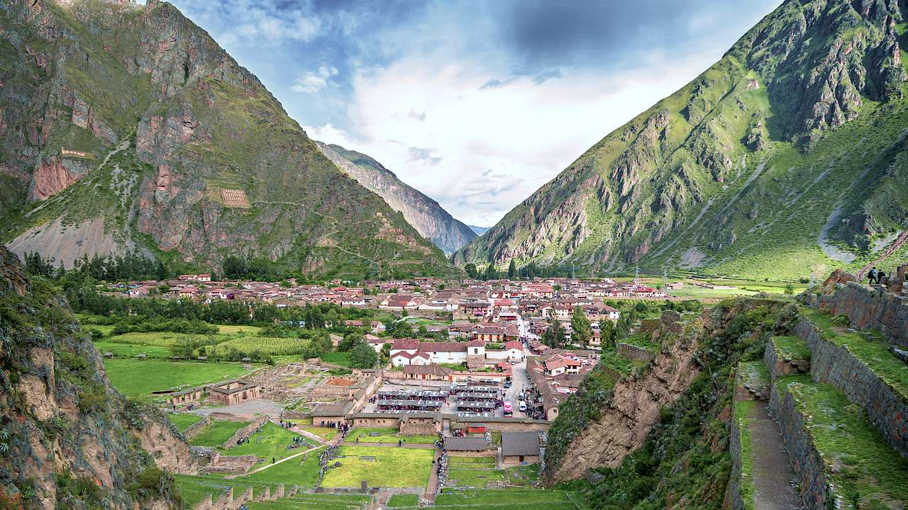 A green valley with low buildings surrounded by mountains and greenery