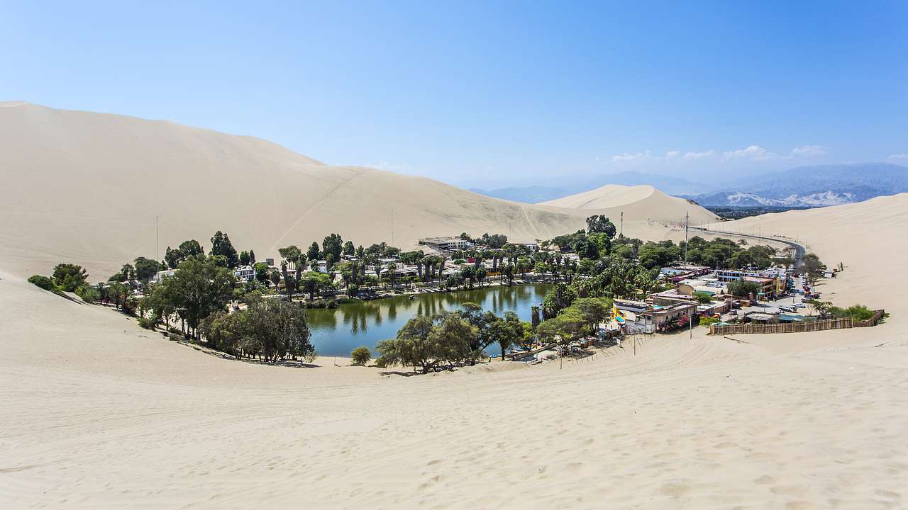 A small town surrounding a pond with trees in the middle of a hilly desert