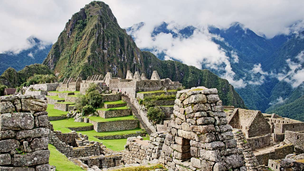 Stacks of old ruins in Machu Picchu with green mountains with clouds at the back