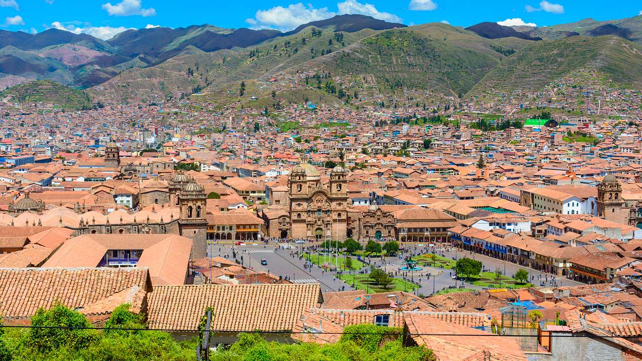 An aerial photo of the brown rooftops of Cusco City with green hills behind