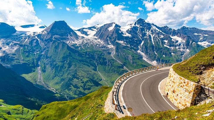 A mountain road next to other mountains covered in snow and greenery