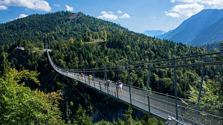 A suspension bridge stretching across a forest under a blue sky with clouds