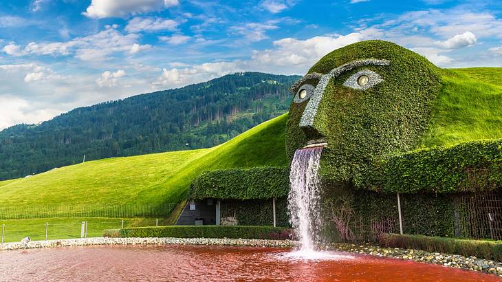 A grass sculpture of a face with a fountain flowing out of the mouth into a red pool