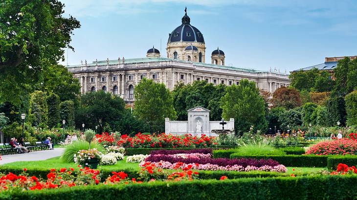 A garden with flower displays and trees next to a palace