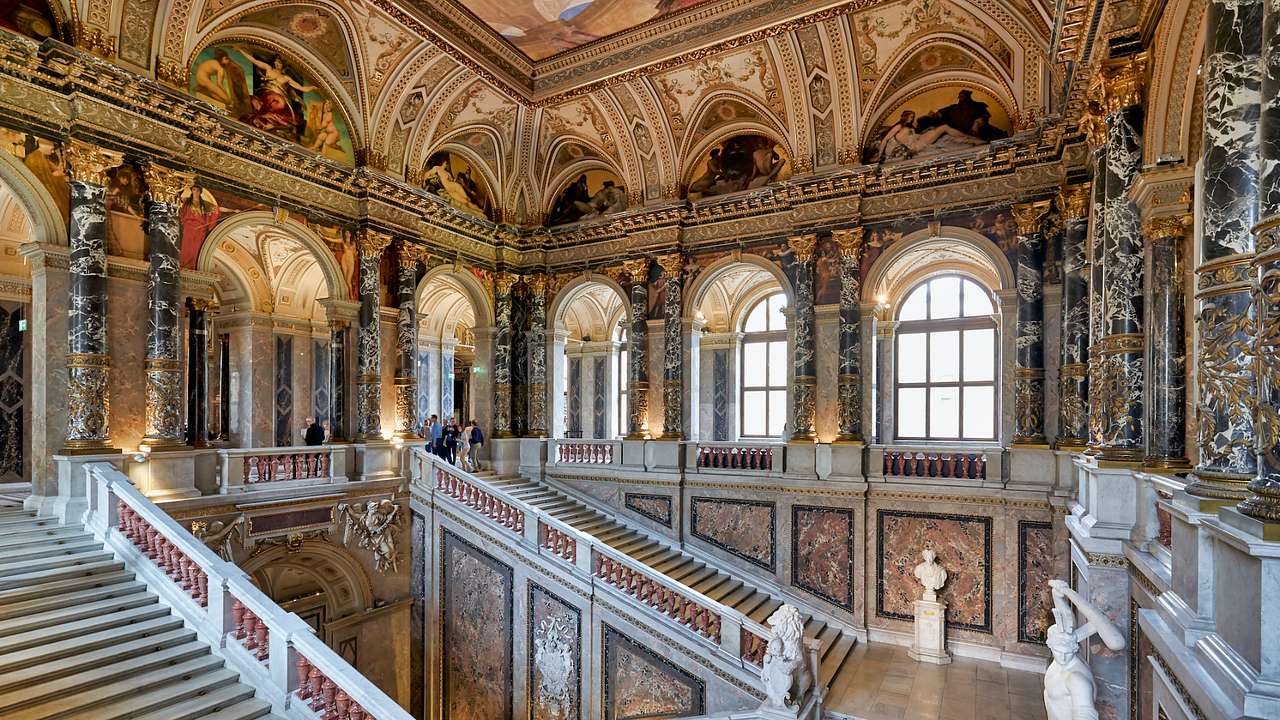 The interior of an art museum with grand staircases, arched windows, and frescoes