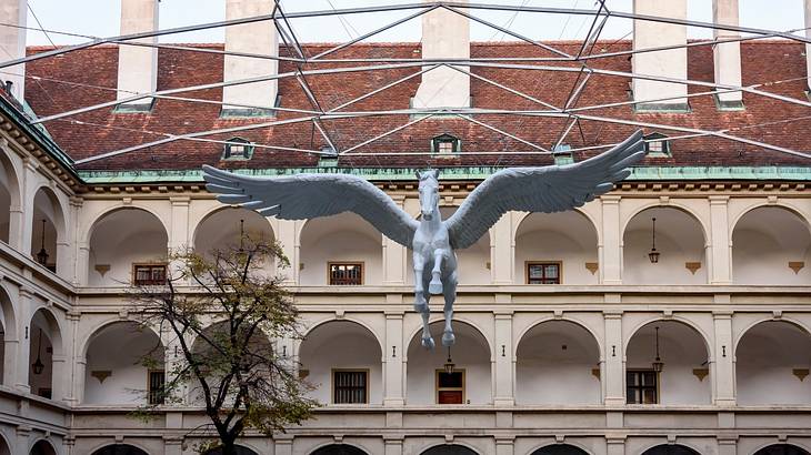 A horse statue with angel wings hanging in front of a building with many arches