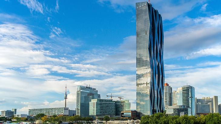 A tall mirrored skyscraper next to smaller city buildings and trees