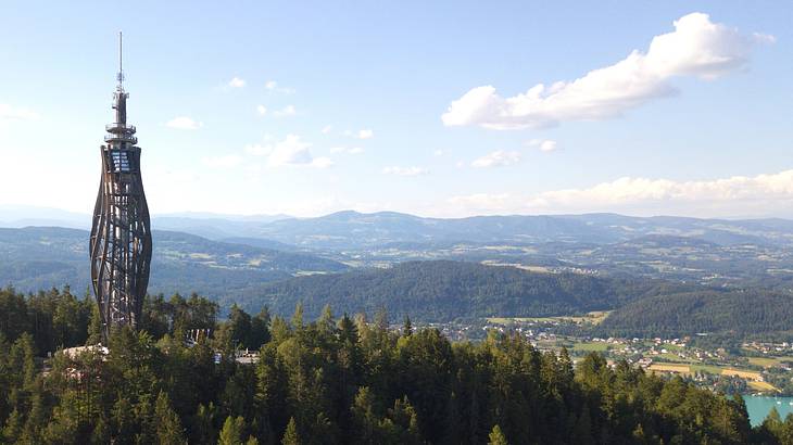 A twisting-style observation tower surrounded by trees and greenery-covered mountains