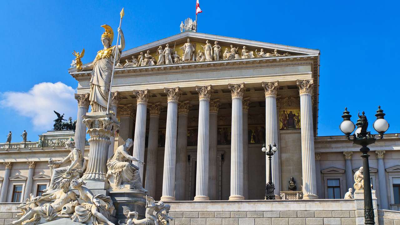 A stone building with columns next to a statue and a clear blue sky