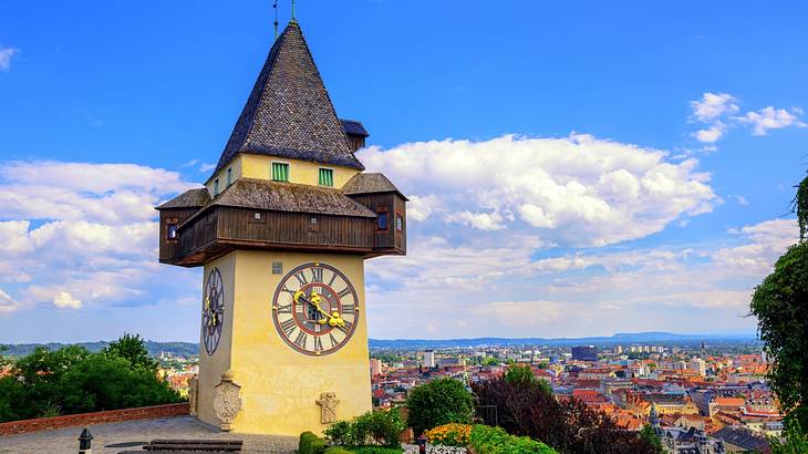 A small clock tower with a pointed roof on a hill above trees and a town