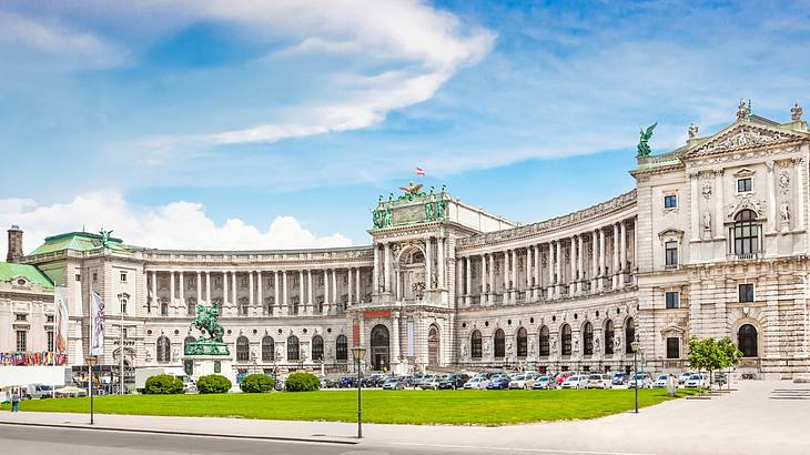 A large white stone palace with columns and grass and a statue in front