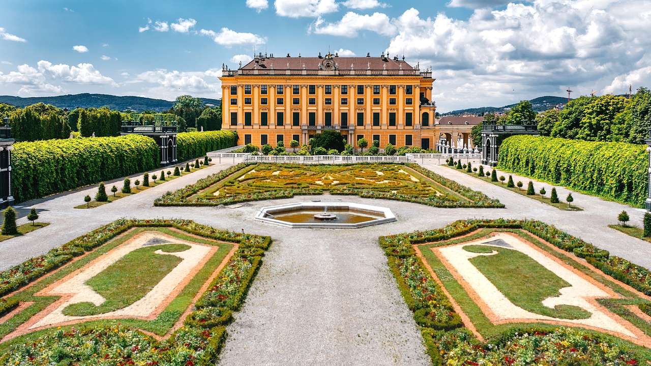 A palace next to a manicured garden with a path and greenery