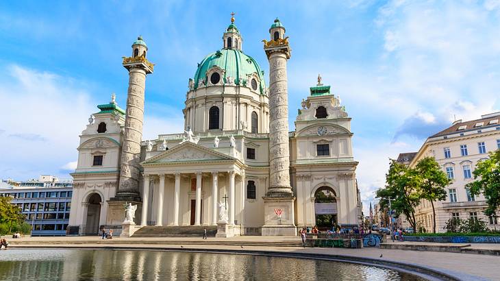 A stone cathedral with columns and a domed roof next to a pond