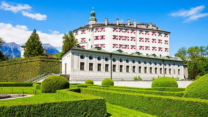 A large white building with red details next to green bushes on a sunny day