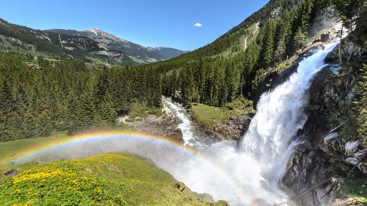 A waterfall flowing down a greenery-covered mountain with a rainbow beneath it