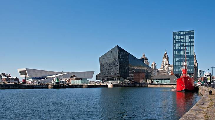 A dock along the water with ships and buildings in the background under a clear sky