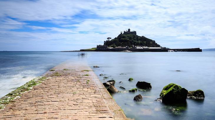 A tree-filled island across a shallow body of water with a castle on top of the hill