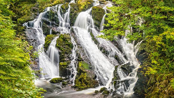 A view of multiple waterfalls cascading down rocks, surrounded by greenery