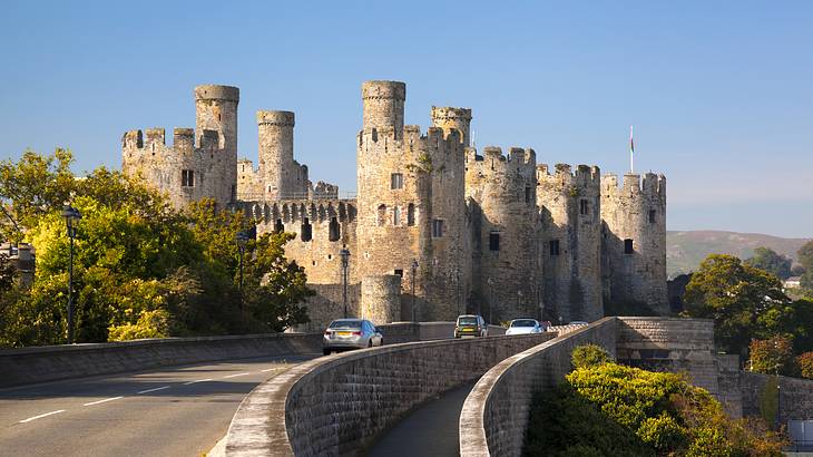 A horizontal view of a stone fortress with a bridge highway and a few cars in front