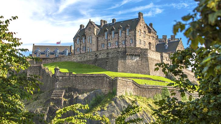 A view of a castle on a hill surrounded by green trees from below