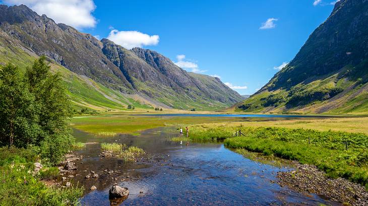 A river running through a green valley between mountains under blue skies with clouds