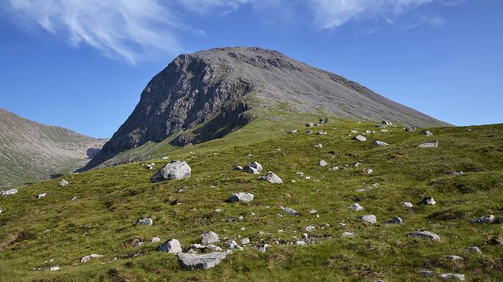 A grassy hill with rocks and a mountain in the background on a sunny day