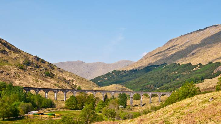 A multi-arched train bridge from afar in between rolling hills on a clear day