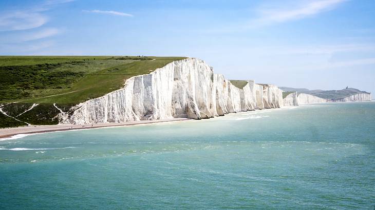 White chalk cliffs with green fields on top, along a coastline, facing a green sea