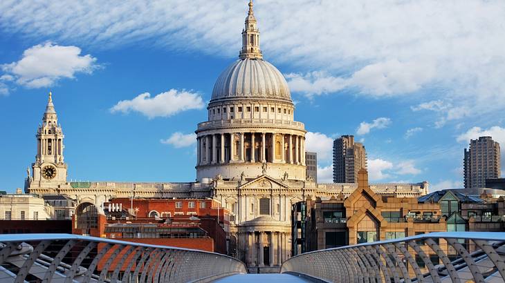 A huge domed cathedral surrounded by buildings and a bridge under a partly cloudy sky