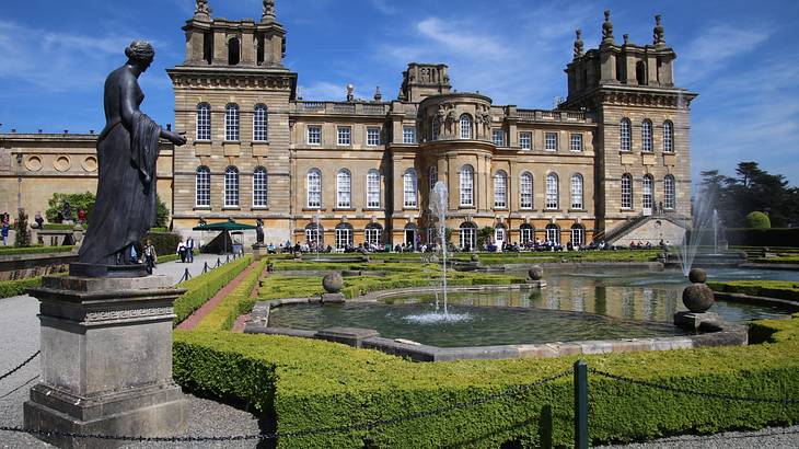 A statue of a woman on the left, with a pond on the right, in front of a grand palace