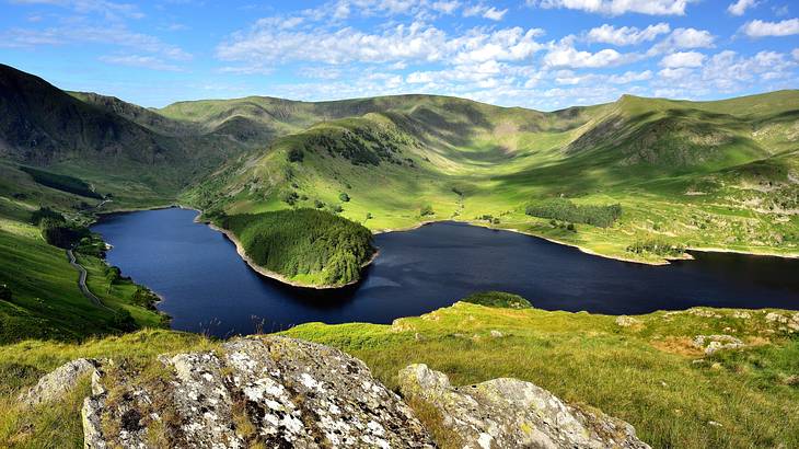 A mountainous landscape with a lake in the middle under partially cloudy blue skies