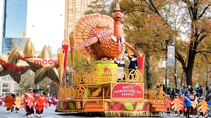 A parade float designed like a turkey surrounded by people walking