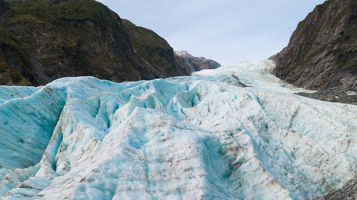 Picture of a massive icy-blue glacier from below between mountains