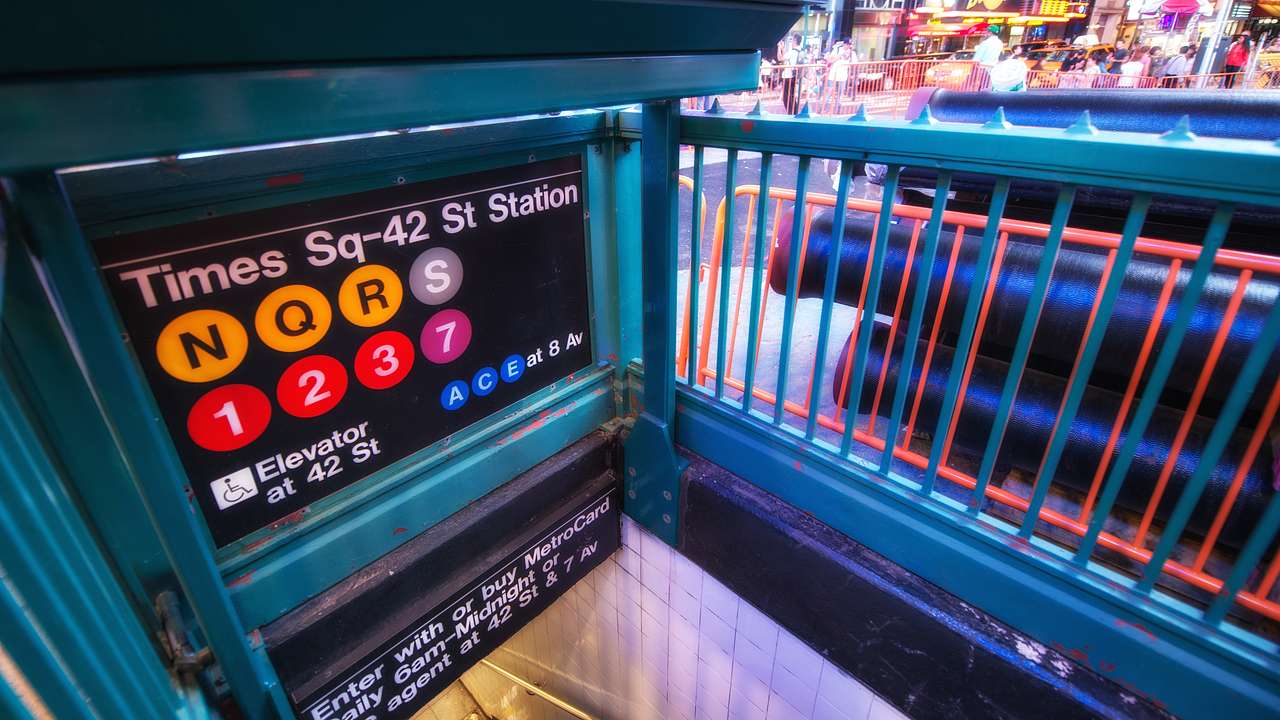 Signage saying "Times Sq-42 Station" near railings and the road