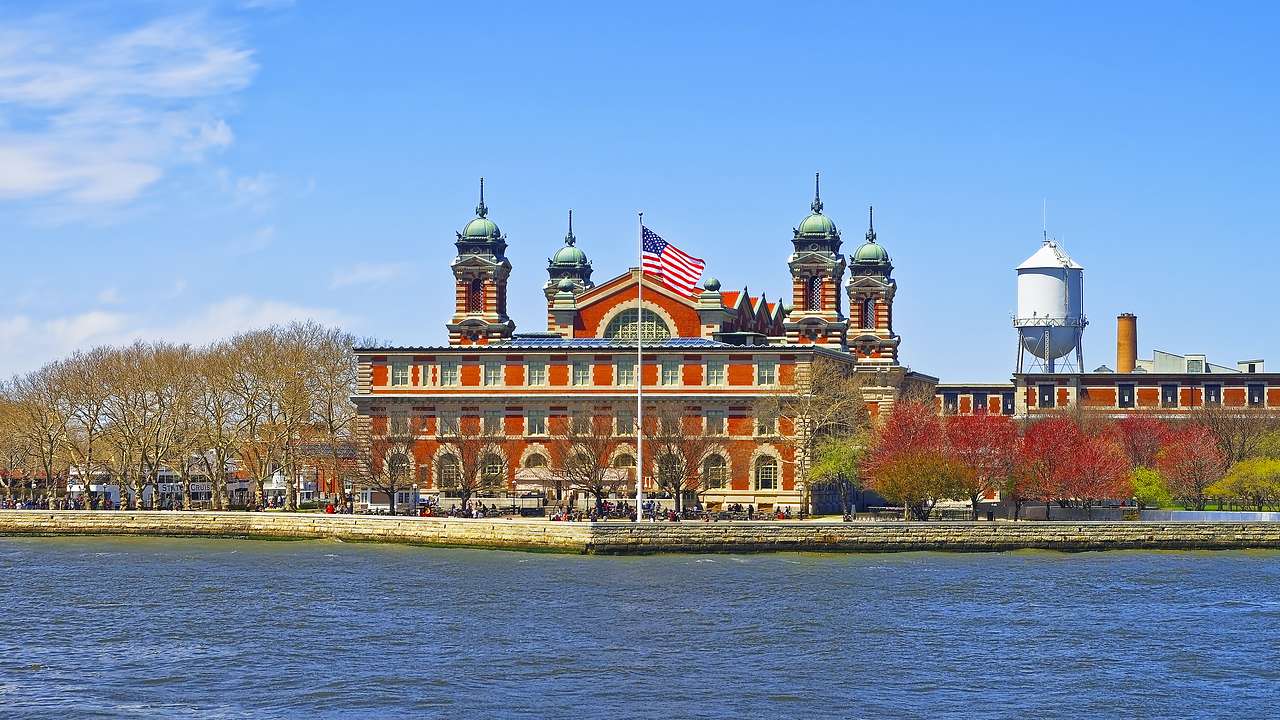 A red building with spires near trees and a body of water