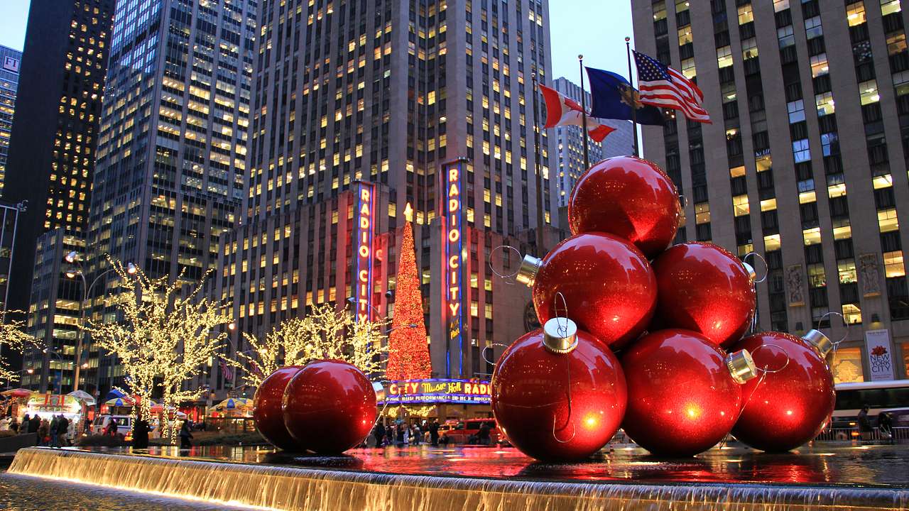 A water fountain with statues of Christmas baubles near skyscrapers lit at night