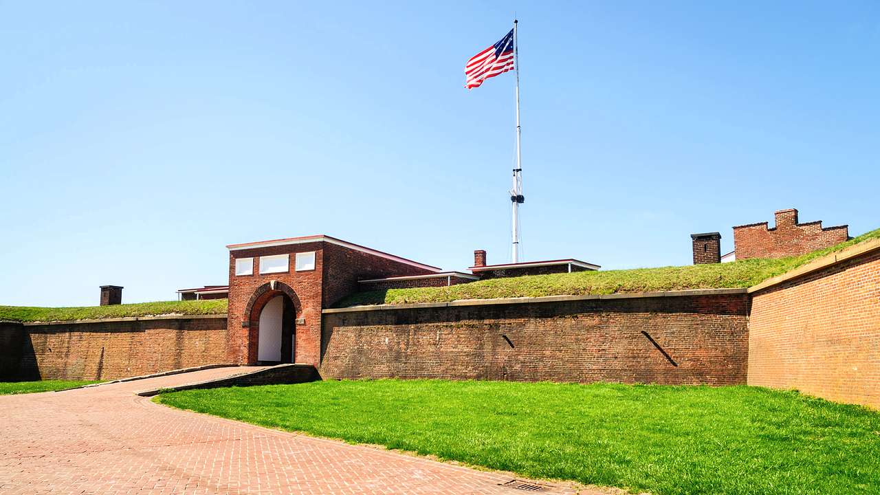 A bricked pathway leading to a bricked archway entrance of a fort with a US flag