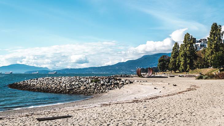 A beach with a partly rocky shore, a U-shaped structure, and ships in the water