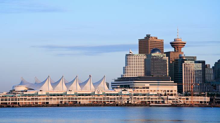 A building with several tent-like roofs on the waterfront with buildings behind it