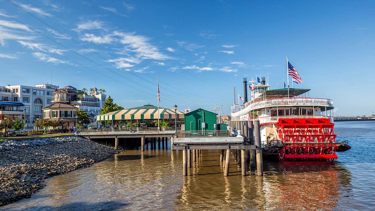 An old-fashioned steamboat on a river with a small pier and buildings to the side