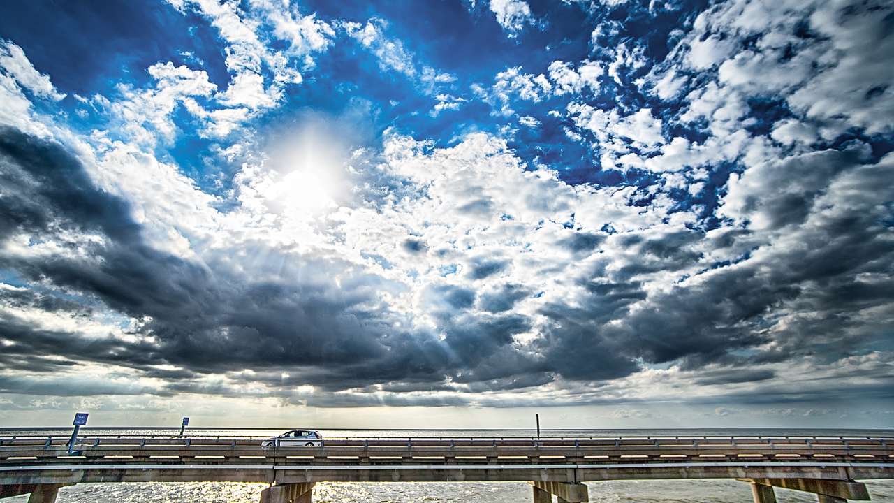 A bridge across the water with a car on it under a blue sky with clouds