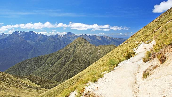 A hiking track going up a mountainside with several mountain ranges at the back