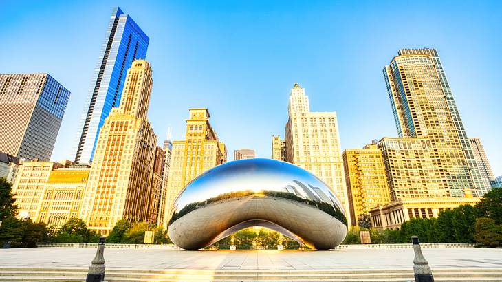 A silver, reflective bean-shaped structure with buildings in the background