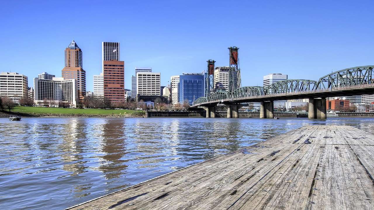 A city skyline with a bridge, water, and a wooden pier in front of it