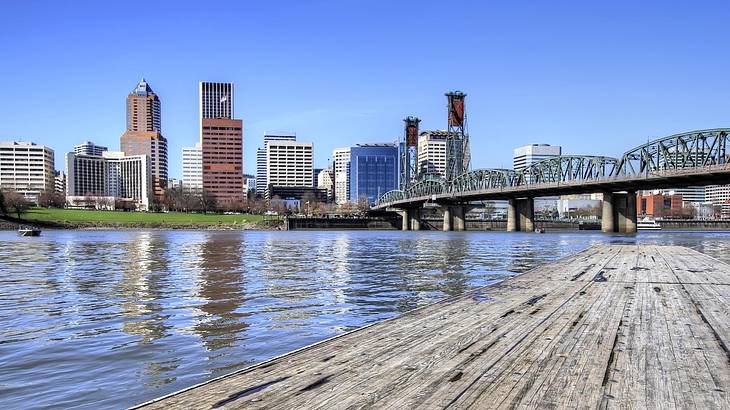 A city skyline with a bridge, water, and a wooden pier in front of it