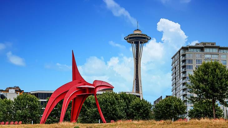 A red sculpture in a park with a building and observation tower behind it