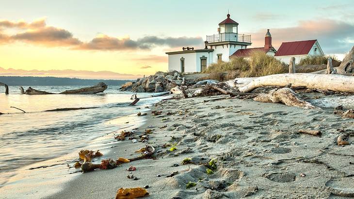 A white and red lighthouse building next to a sandy shore and the ocean at sunset