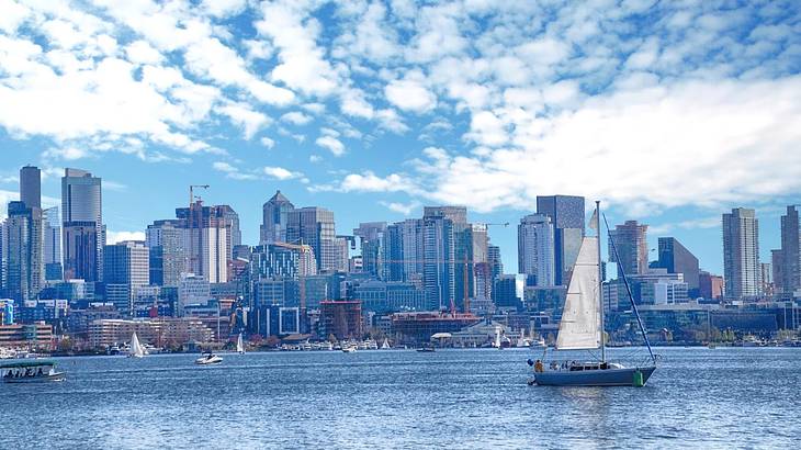 A sailboat on the water with a city skyline behind it under a cloudy sky