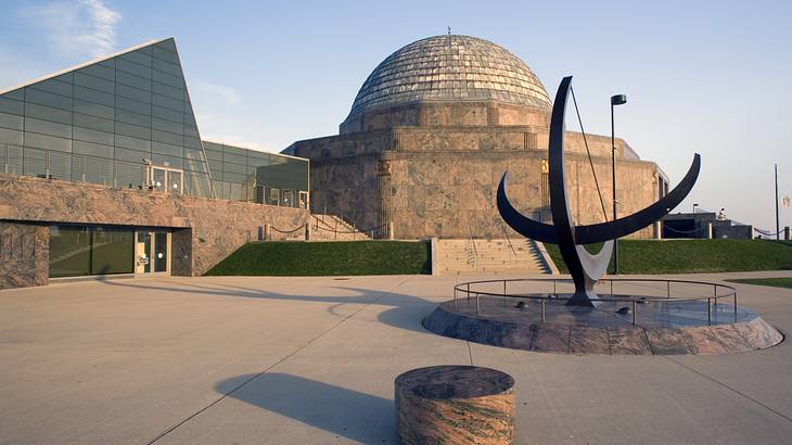 A sculpture with two intersecting crescent shapes and two buildings in the background